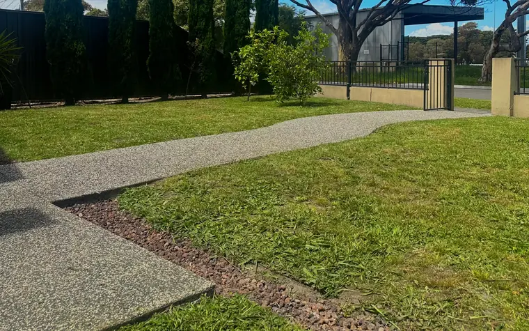 A front lawn cut back cleanly to a concrete path and a pebbled garden edge